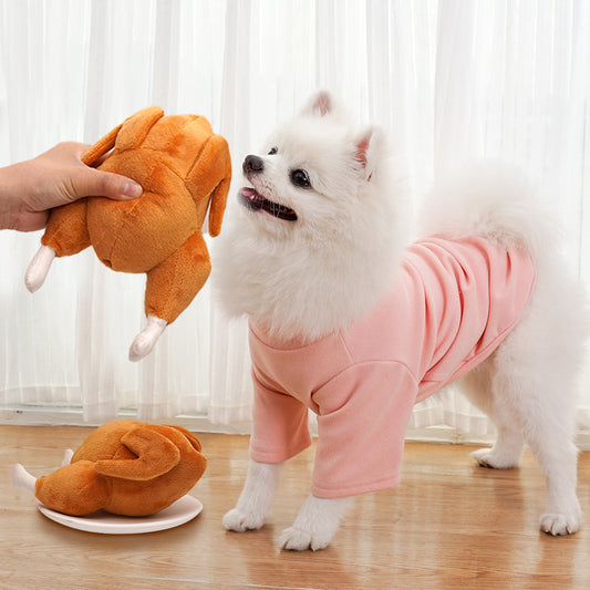 White Pomeranian dog playing with squeaky roast chicken plush toy on wooden floor