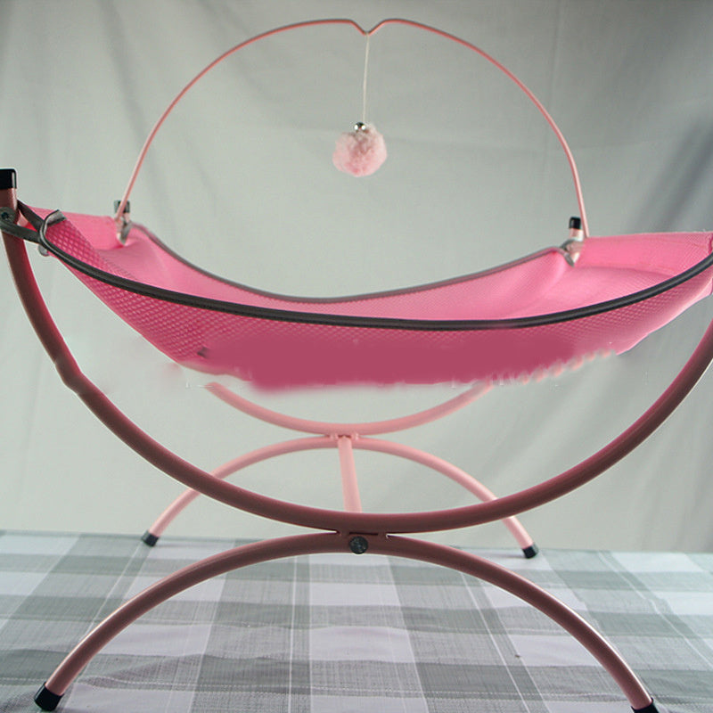 A pink, fluffy cat bed with a dangling pom-pom nearby.